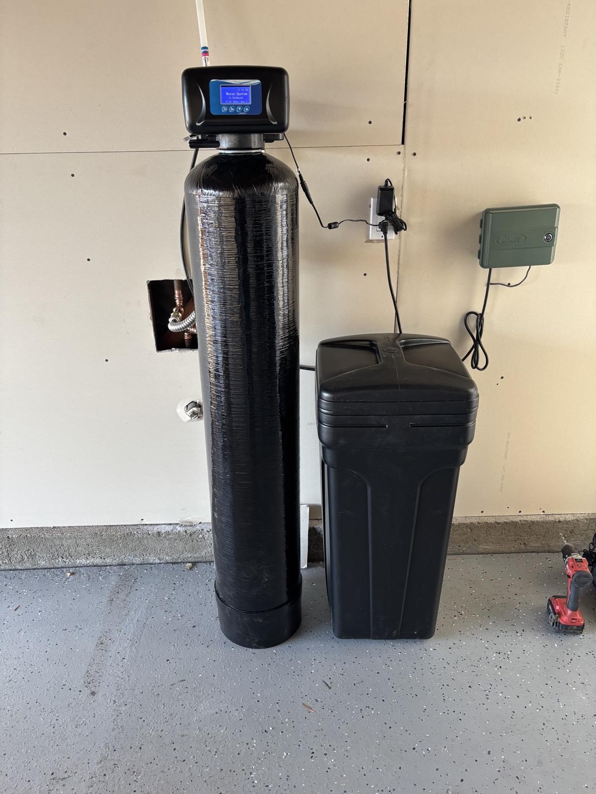 Under-sink reverse osmosis system with filter housings and a white storage tank installed next to a garbage disposal, with tubing routed neatly along the cabinet