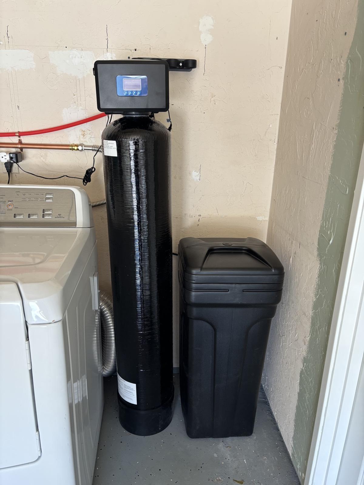 Whole-home softening system and brine tank installed in a garage laundry area, plumbed into the main line with copper connections